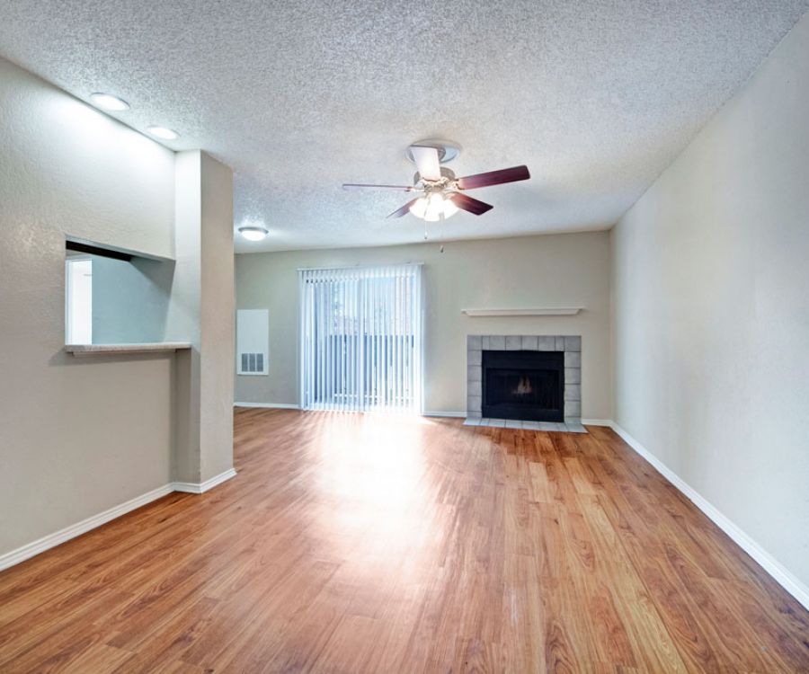 Quail Crossing Spacious empty living room with wooden floor, ceiling fan, fireplace, and sliding glass doors to a balcony.