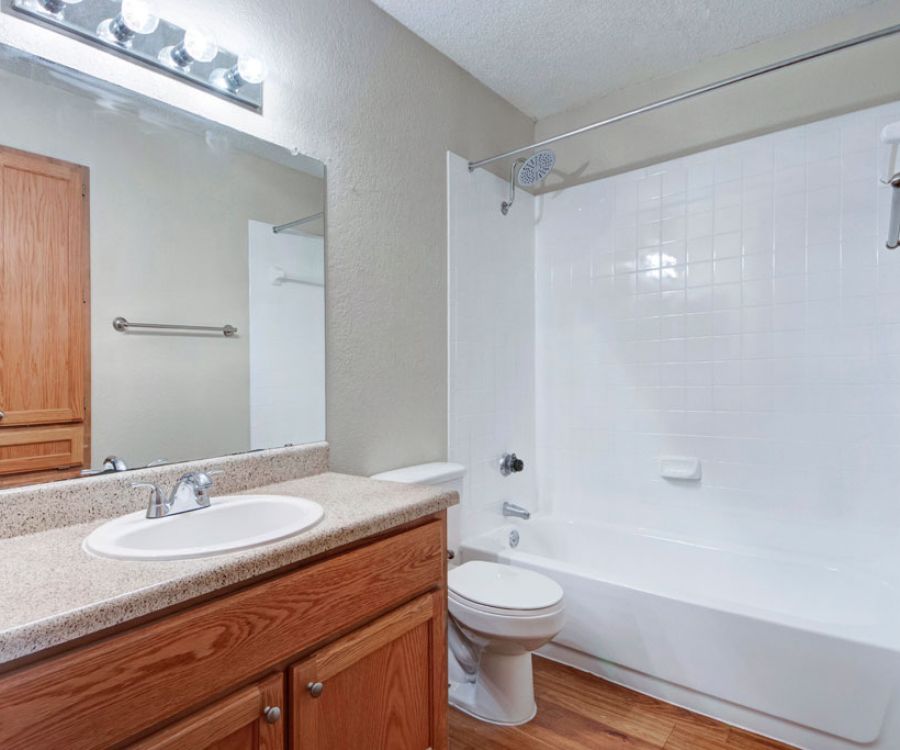 Quail Crossing A clean bathroom with a bathtub, shower, toilet, wooden cabinets, and a large mirror above the sink.