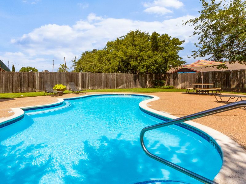 Quail Crossing A sparkling outdoor pool with lounge chairs, a wooden fence, and trees in the background under a partly cloudy sky.