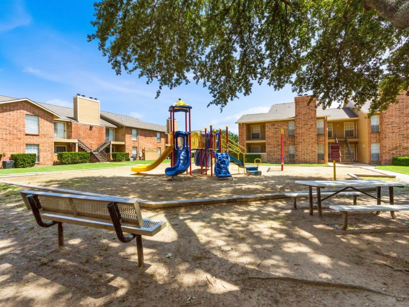 Quail Crossing Playground with slides and climbing structures surrounded by brick apartments under a clear blue sky.