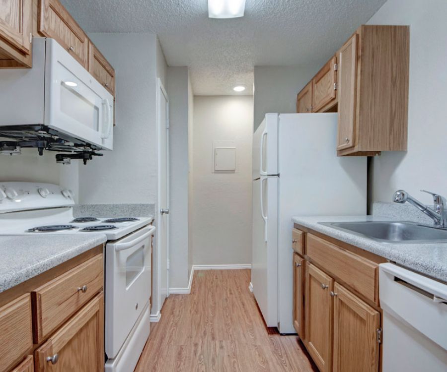 Quail Crossing Compact kitchen with wooden cabinets, white appliances, and light wood flooring.