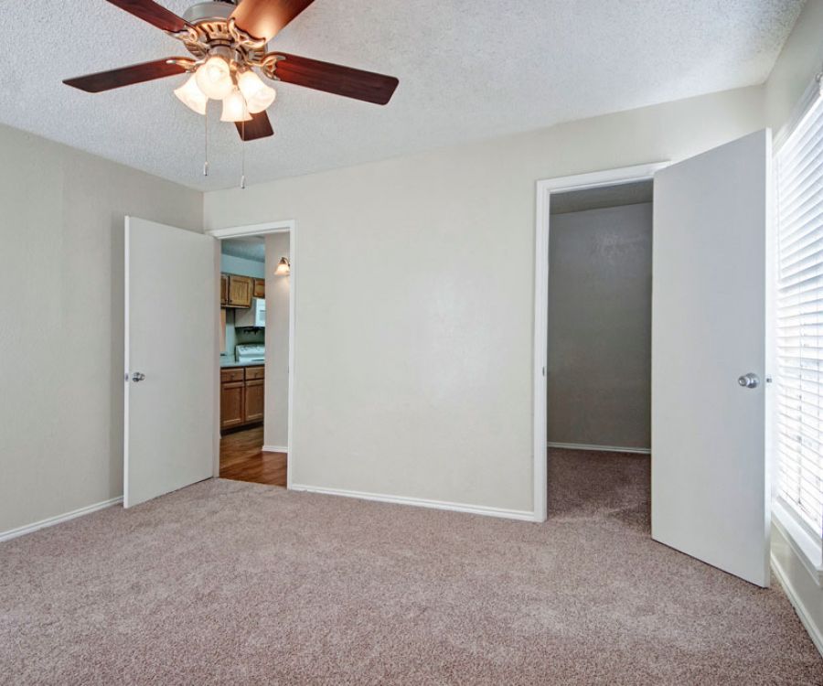 Quail Crossing Empty room with beige carpet, ceiling fan, and open doors leading to kitchen and another room.